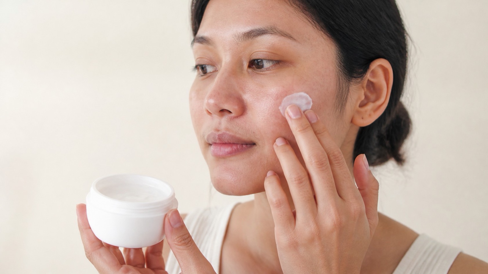 A woman gently applying a plain moisturiser to her cheek